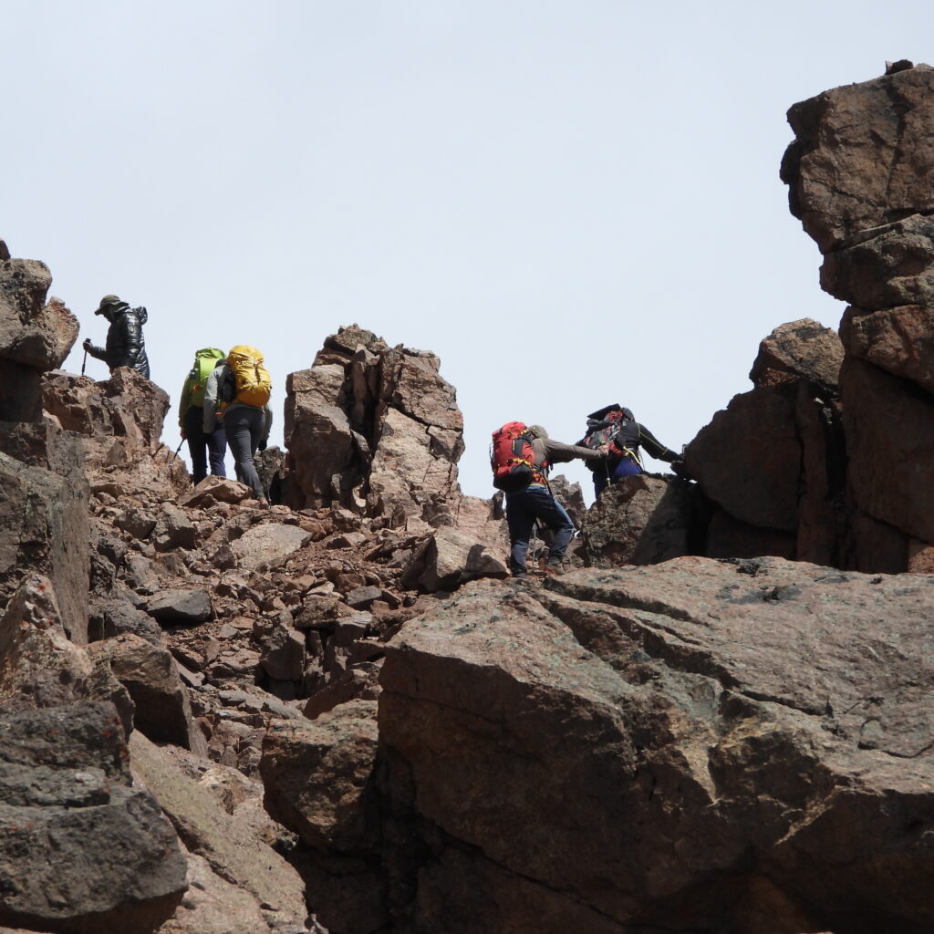 Group of trekkers climbing over steep rocky terrain in Mount Kenya’s alpine zone en route to Austrian Hut on the Chogoria–Sirimon route