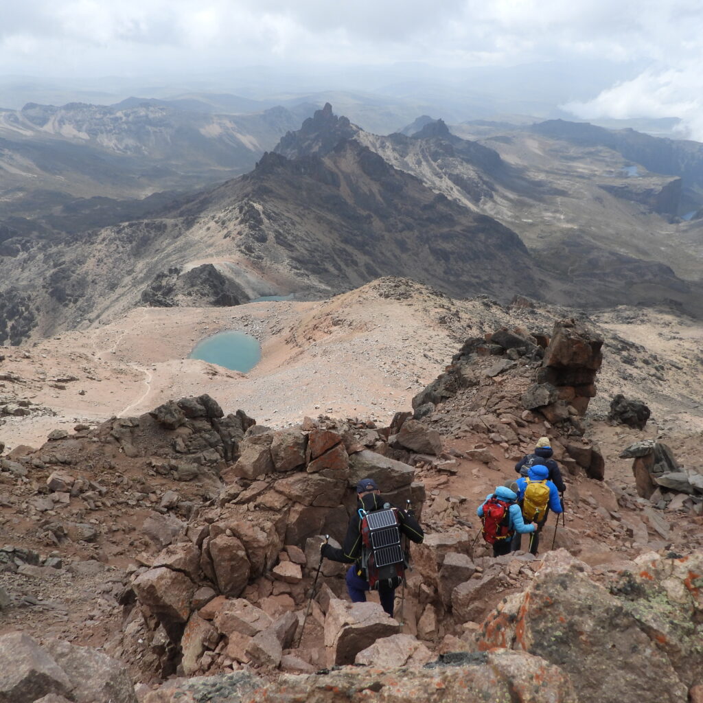 Trekkers descending from Point Lenana on Mount Kenya with views of alpine tarns and Gorges Valle