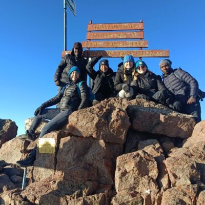 Trekking group celebrating at the Point Lenana summit sign, 4,985m, on Ahambi Tours' 6-Day Mount Kenya Sirimon–Chogoria trek"