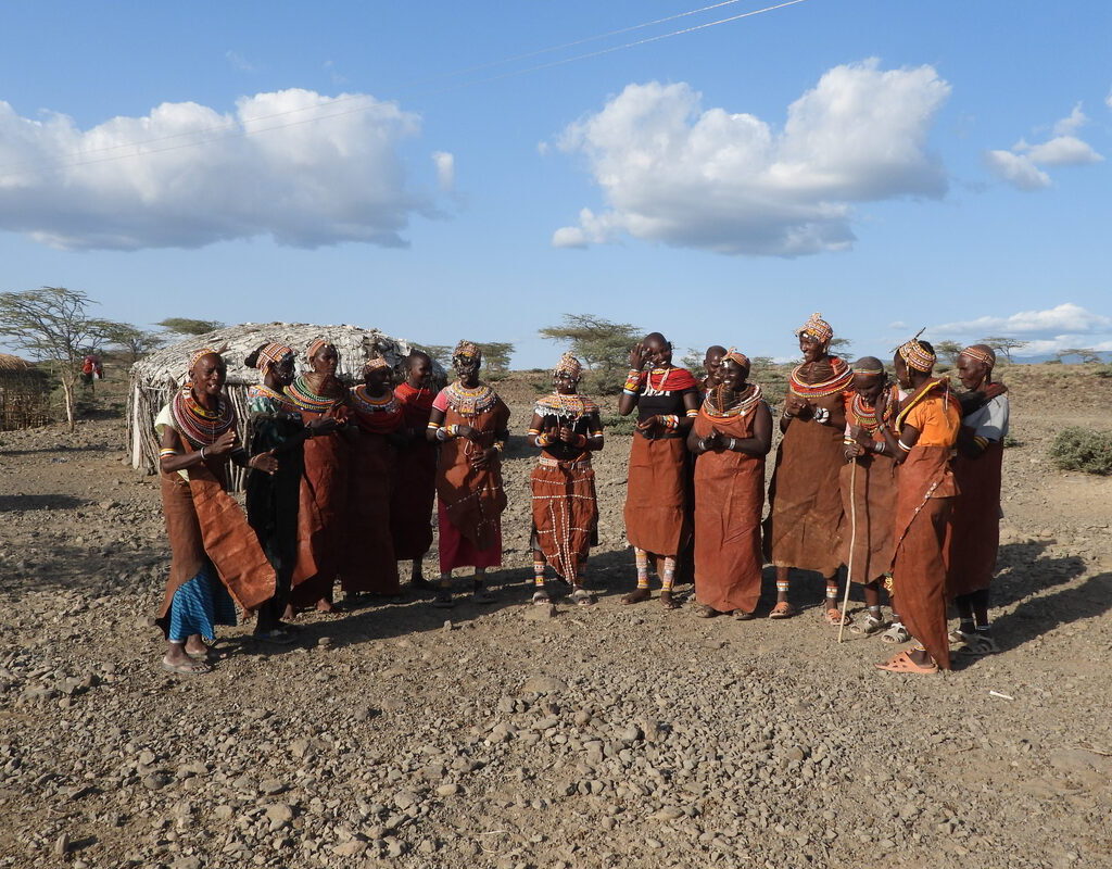 Rendile women in traditional ochre leather dress and colourful beadwork headdresses gathered outside a thatched manyatta homestead in the Kenyan desert