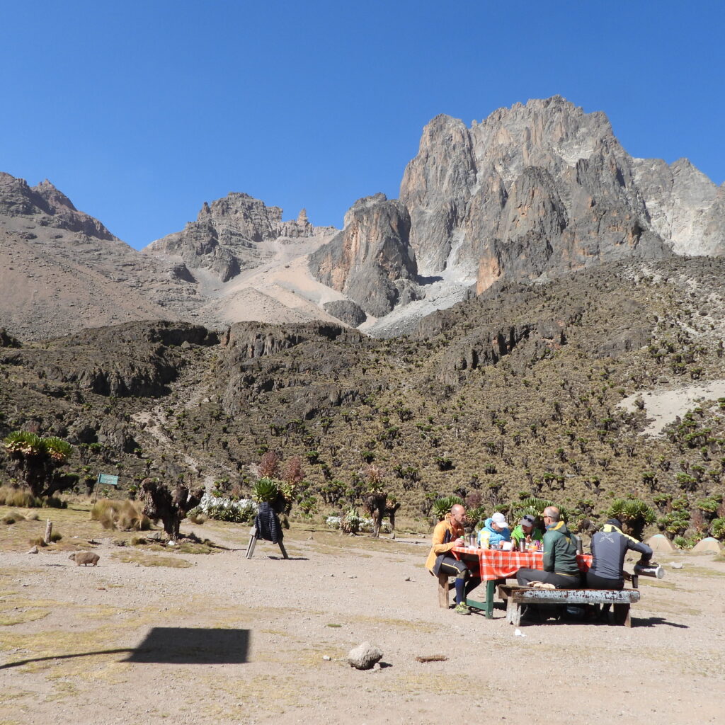 Trekkers enjoying an outdoor meal at Shipton’s Camp with panoramic views of Mount Kenya’s Batian and Nelion peaks