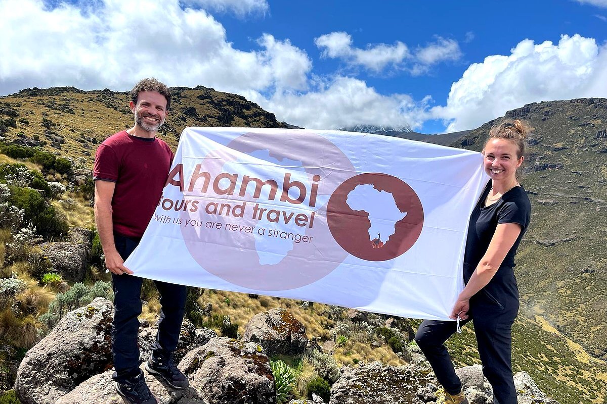 Two trekkers holding Ahambi Tours flag on Mount Kenya moorland