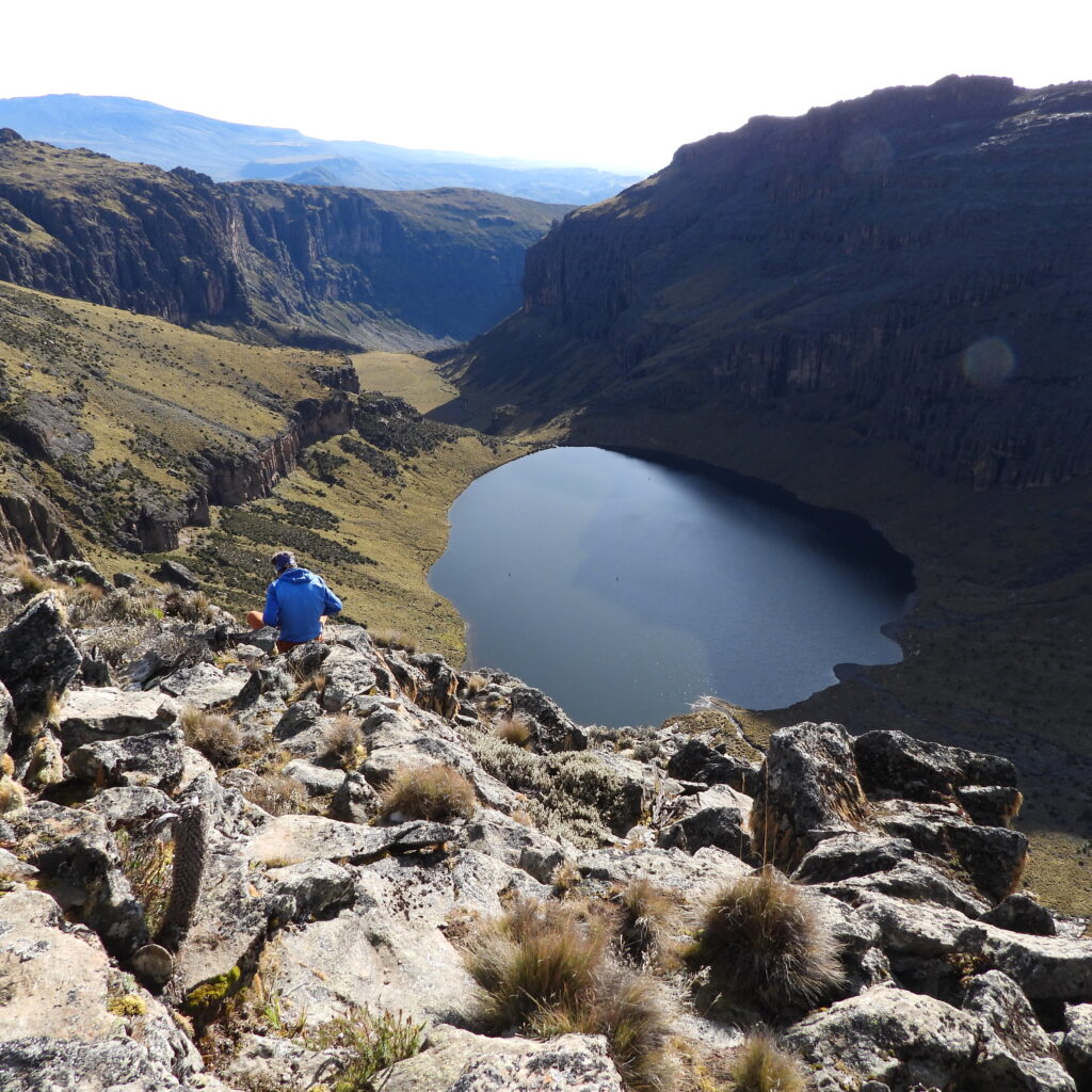 Hiker overlooking Lake Michaelson on Mount Kenya’s Chogoria Route, surrounded by rugged cliffs and alpine valleys